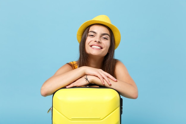 Donna turistica viaggiatrice in abiti casual gialli, cappello con macchina fotografica valigia su blu