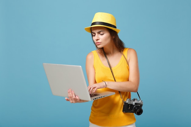 Donna turistica viaggiatrice in abiti estivi gialli, cappello con computer pc portatile su blu