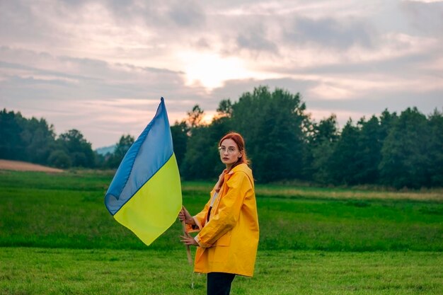 Donna ucraina nel campo con una grande bandiera dell'Ucraina Foto patriottiche Bella donna in un impermeabile giallo