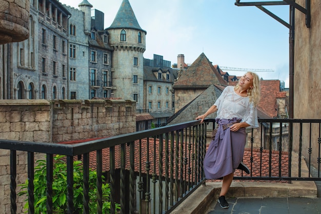 Donna un adulto giovane bella e felice bionda su un balcone sullo sfondo di una vecchia bella città europea