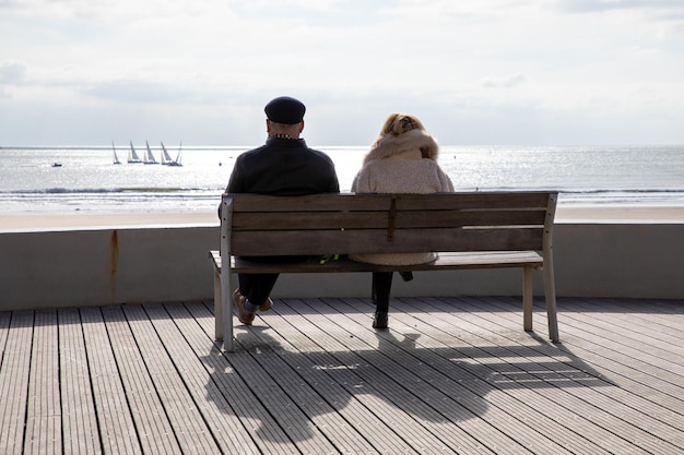 Donna uomo coppia senior seduta panchina fronte spiaggia costa e godendo guarda il mare