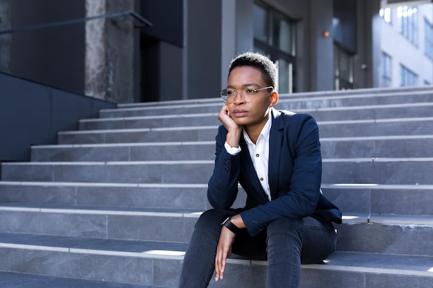 Donna uomo d'affari in bancarotta depressa seduta sulle scale vicino all'ufficio Donna afroamericana ha perso il lavoro durante la crisi economica