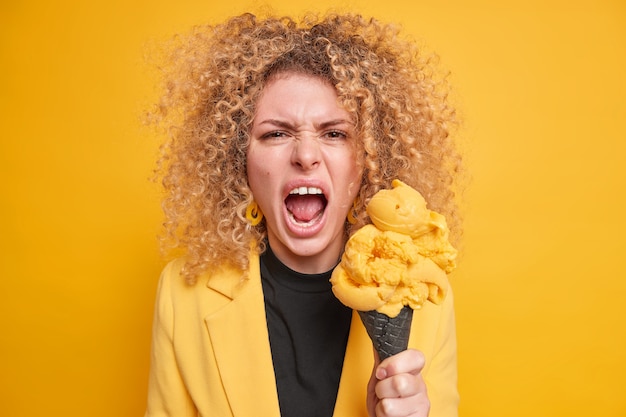 donna urla con rabbia tiene la bocca aperta tiene il gelato esprime emozioni e sentimenti negativi vestita con una giacca elegante ha un debole per i dolci mangia cibo spazzatura ricco di calorie