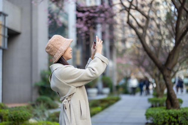 Donna usa il cellulare per scattare una foto all'albero di sakura