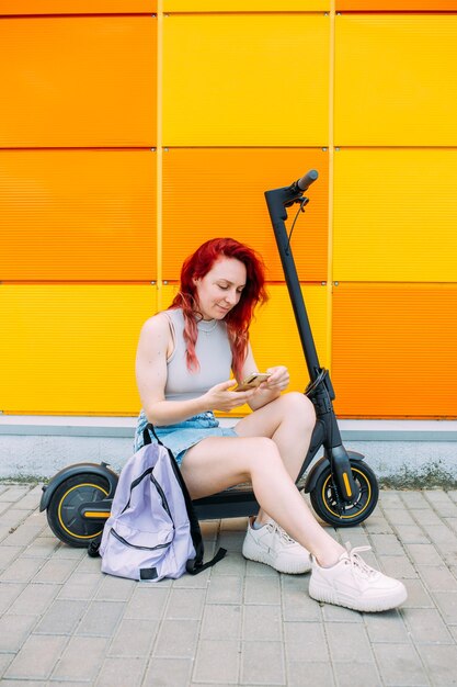 Donna usa uno smartphone e uno scooter elettrico in estate in città