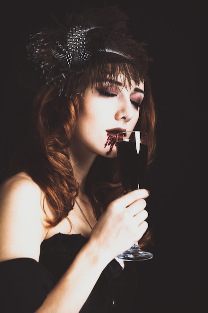 Donna vampiro rossa con bicchiere di sangue. Foto in stile vintage.