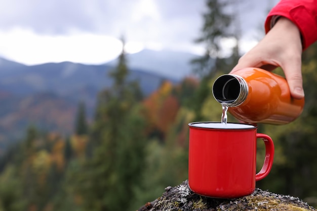 Donna versando acqua calda dalla bottiglia termica nella tazza in montagna primo piano Spazio per il testo