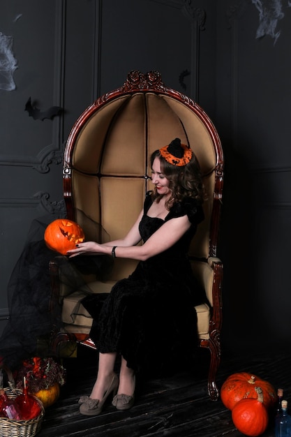 donna vestita di nero seduta su una sedia sorridente con in mano decorazioni di zucca spettrali di Halloween