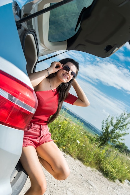 Donna viaggiante felice che si siede nel bagagliaio dell'auto e che riposa in sosta in campo rurale. stile di vita estivo