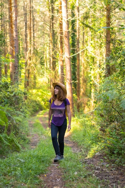 Donna viaggiatrice che indossa un cappello e guarda i pini della foresta