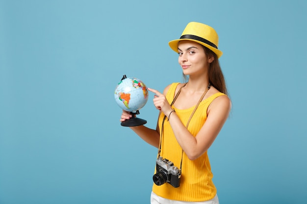 Donna viaggiatrice in abiti casual estivi gialli e cappello con globo e macchina fotografica su blu