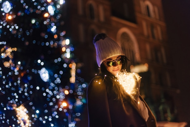 Donna vicino a un albero di Natale sulla strada con ghirlande nelle sue mani