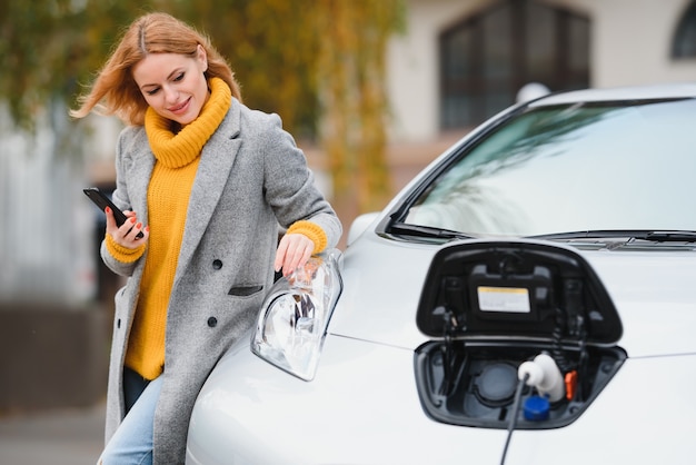 Donna vicino a un'auto elettrica a noleggio. Veicolo caricato alla stazione di ricarica.