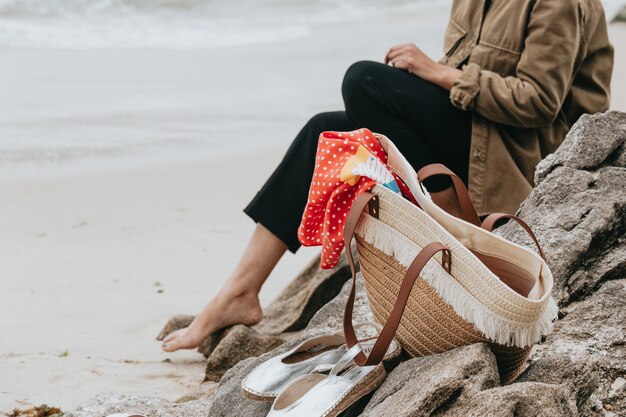 Donna vicino ad alcuni sandali e una borsa estiva in spiaggia durante una giornata di sole