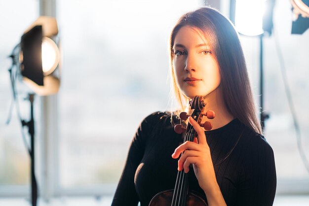 Donna violinista ispirata Ripresa professionale Artista musicista Studio fotografico Elegante signora sorridente con violino in mano che guarda l'obbiettivo in riflettori luci calde sullo sfondo