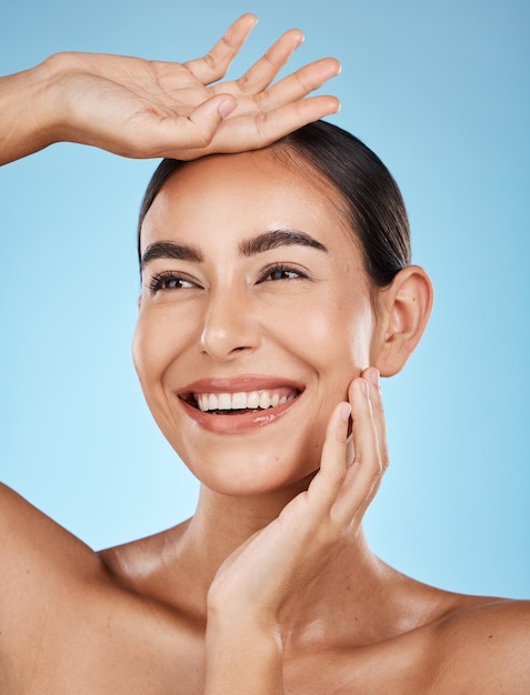 Donna viso e sorriso felicità e bellezza con cosmetici naturali e bagliore isolato su sfondo blu Cura cosmetica pulita e mani con trucco facciale e pelle sana con cura della pelle in studio