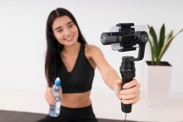 Donna vlogging a casa durante l'allenamento e tenendo la bottiglia d'acqua