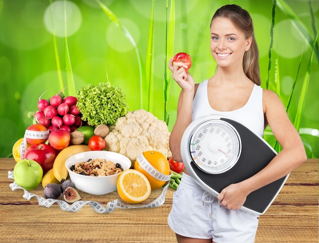 Donne a dieta che tengono bilancia, cibo sano sullo sfondo