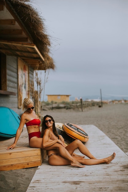 Donne abbastanza giovani in bikini che si siedono vicino alla cabina del surf su una spiaggia al giorno d'estate