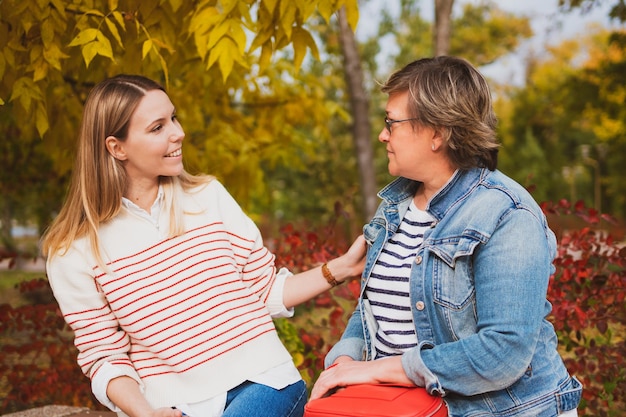 Donne affascinanti mamma e figlia sono sedute su una panchina nel bellissimo parco e parlano tra loro