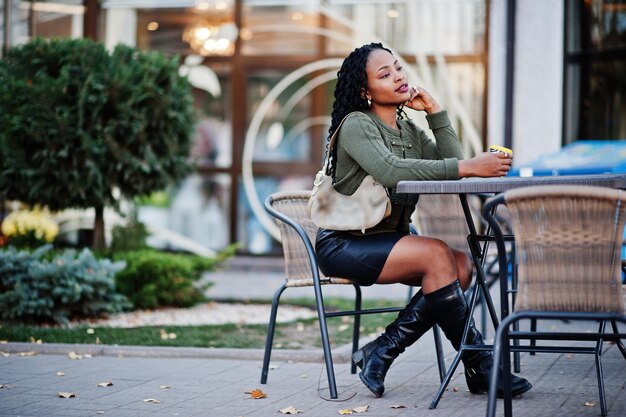 Donne afroamericane alla moda alla moda in maglione verde e gonna nera poste caffè all'aperto seduti al tavolo con una tazza di caffè