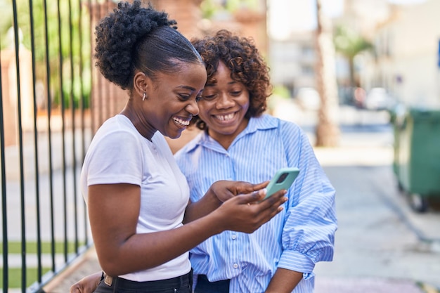 Donne afroamericane madre e figlia che utilizzano smartphone in strada