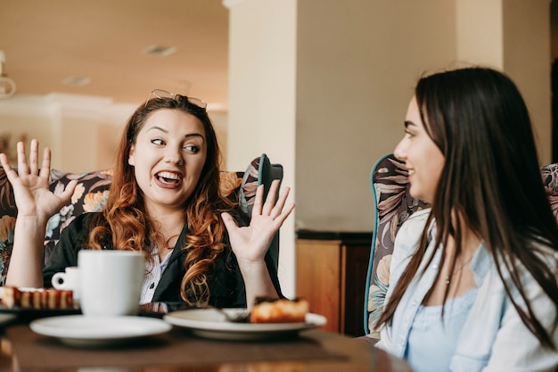 Donne allegre con i capelli rossi che raccontano storie alla sua amica mentre erano seduti in un caffè.