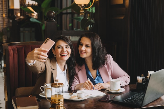 Donne allegre in tailleur che scattano foto con il telefono cellulare