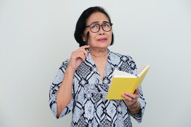 Donne anziane asiatiche che pensano a qualcosa mentre tengono un libro e una penna