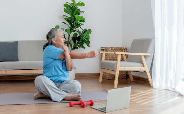 Donne anziane asiatiche stanno praticando lo yoga nella posizione di base nel suo salotto, che è un esercizio di riscaldamento e meditazione per gli anziani.