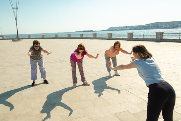 Donne anziane che fanno allenamento sportivo con un allenatore in un parco pubblico, fitness ricreativo dopo la malattia. Donna pensionata che ha uno stile di vita sano con allenamento sportivo.