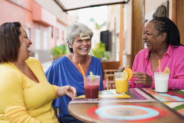 Donne anziane multietniche che si divertono a giocare a indovinare insieme al bar all'aperto