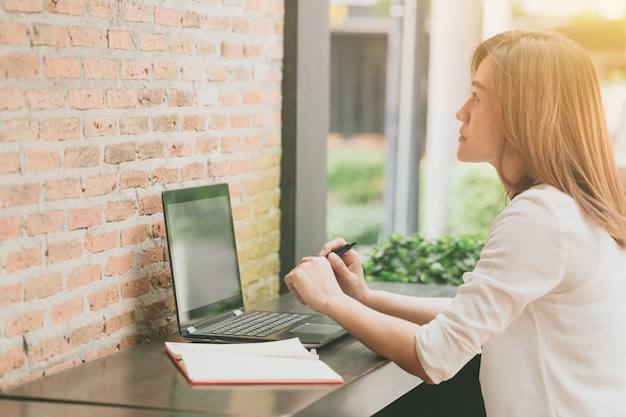 Donne asiatiche che guardano alla parete quando lavorano al caffè con il computer portatile.