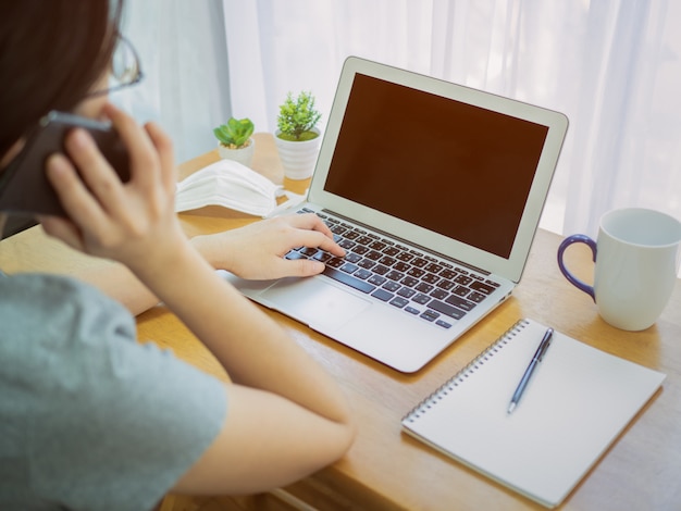 Donne asiatiche che indossano maschere che lavorano a casa e team di conferenza utilizzando notebook e smartphone