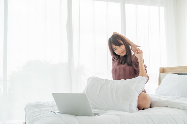 Donne asiatiche che lavorano con il computer portatile sul letto a casa