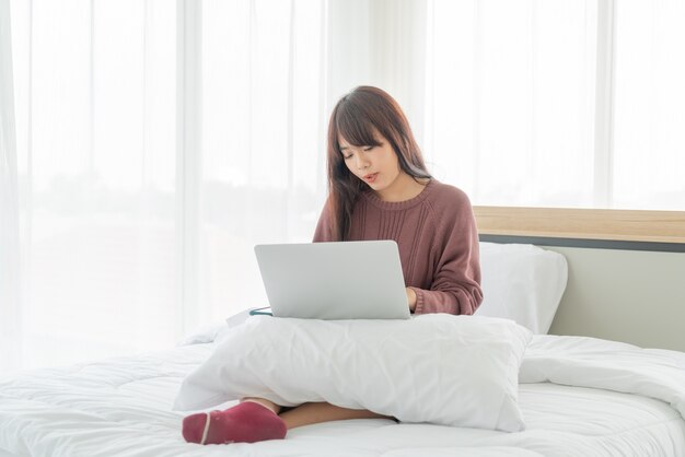 Donne asiatiche che lavorano con il computer portatile sul letto a casa