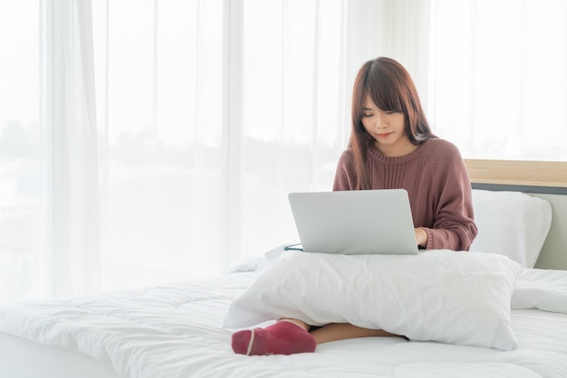 Donne asiatiche che lavorano con il computer portatile sul letto a casa