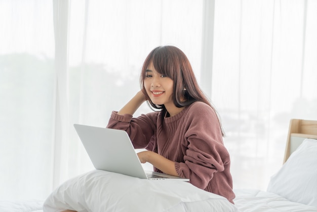 Donne asiatiche che lavorano con il computer portatile sul letto