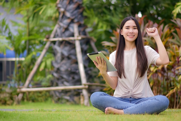 Donne asiatiche che tengono compressa sulla rete sociale e che comperano online da Internet che si siede nel parco della città