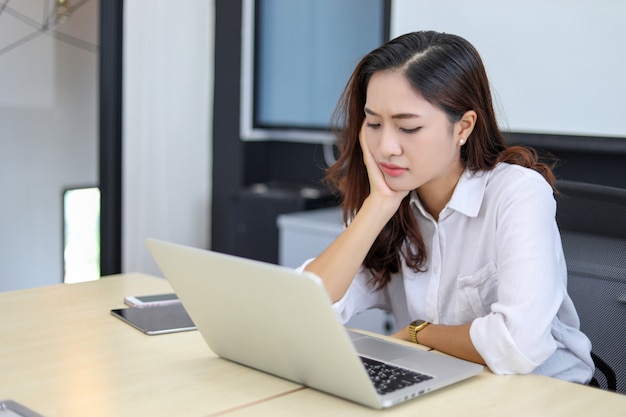 Donne asiatiche di affari che per mezzo del taccuino e serio ed emicrania per lavorare