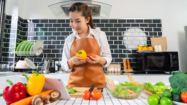 Donne asiatiche felici che cucinano cibo sano mentre guardano la ricetta sulla tavoletta digitale