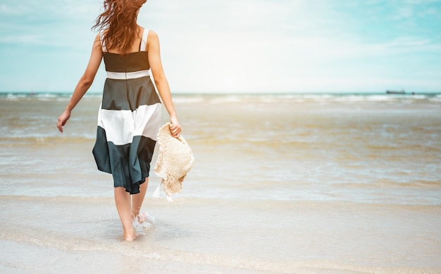 Donne asiatiche felici con cappello in mano che camminano a piedi nudi per ricevere il vento e godersi la vita in vacanza al mare. spiaggia, estate, liftstyle, umore positivo, viaggio, concetto di relax.