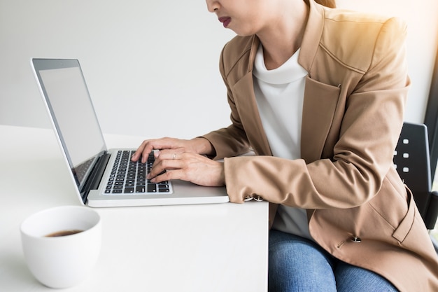 Donne attraenti in attività casual seduto a un tavolo lavorando sul suo computer portatile presso l&#39;ufficio di fronte a una finestra.