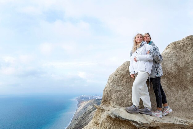 Donne belle in piedi su un'alta montagna sulla costa del mare in una giornata di sole bionde sorridenti che si abbracciano stile di vita attivo e ricreazione altezza piena