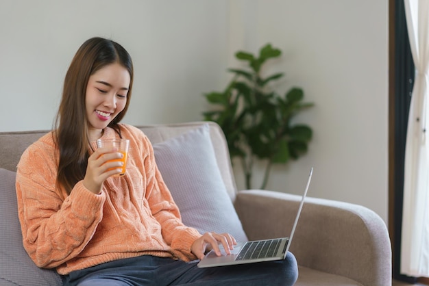 Donne che bevono succo d'arancia e lavorano per digitare un piano aziendale sul portatile nello stile di vita a casa