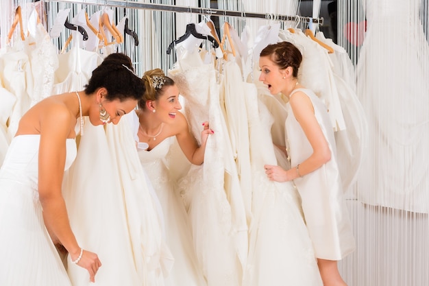 Donne che si divertono durante il montaggio dell'abito da sposa nel negozio di moda per matrimoni