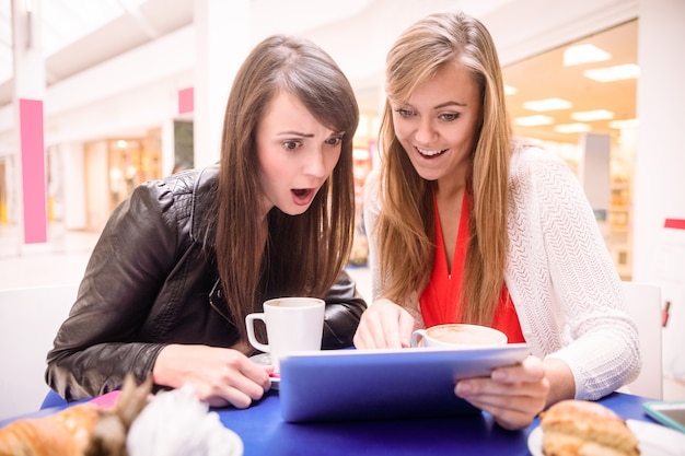 Donne che usano la tavoletta digitale mentre mangiano caffè e spuntini