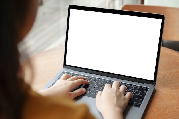 Donne che utilizzano computer portatile con lo schermo in bianco alla tavola nell'ufficio, vista posteriore delle mani delle donne di affari occupate facendo uso del computer portatile alla scrivania.