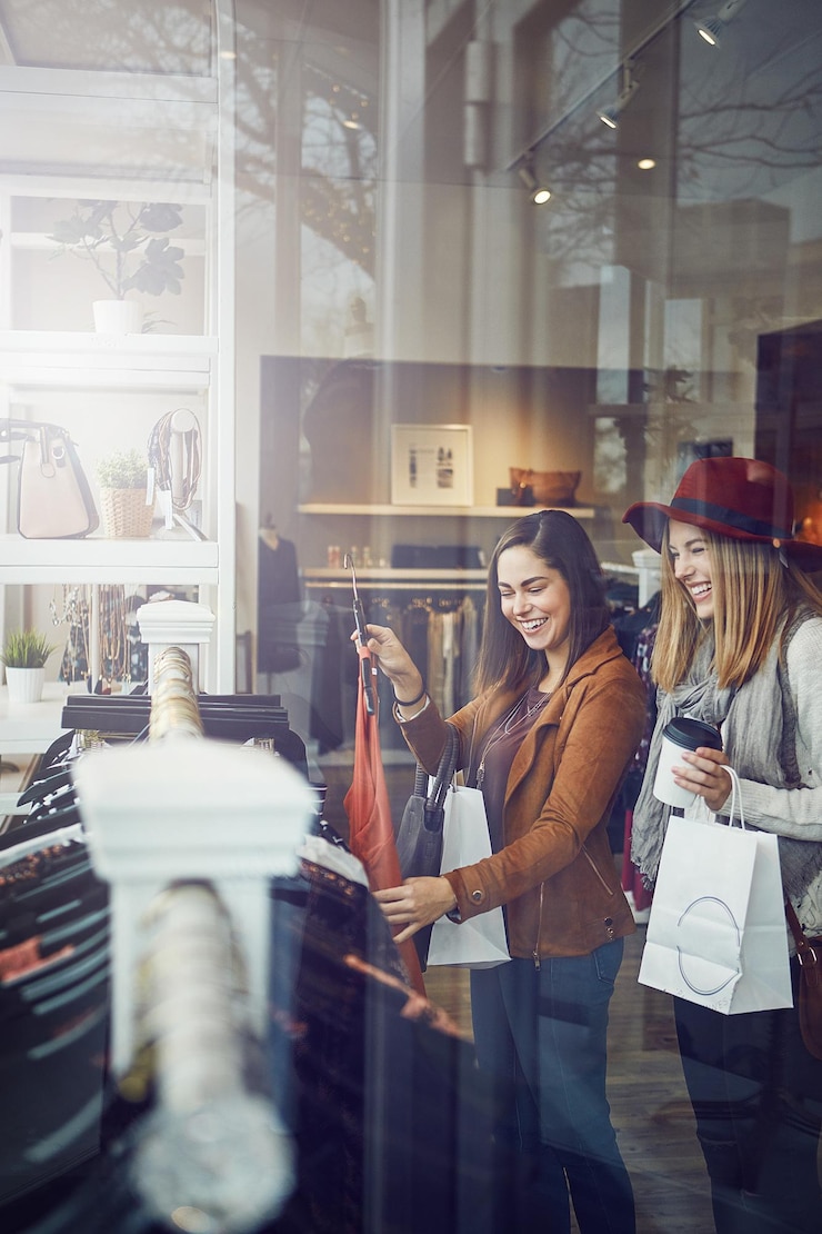 Foto donne clienti e felici con l'abito in un negozio boutique per la promozione sconto e vendita sorrisi amiche e persone che controllano scaffale di vestiti in materiale tessuto e negozio al dettaglio al centro commerciale coperto