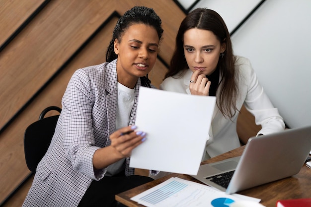 Donne d'affari al lavoro che discutono di affari con un computer portatile e documenti nelle loro mani